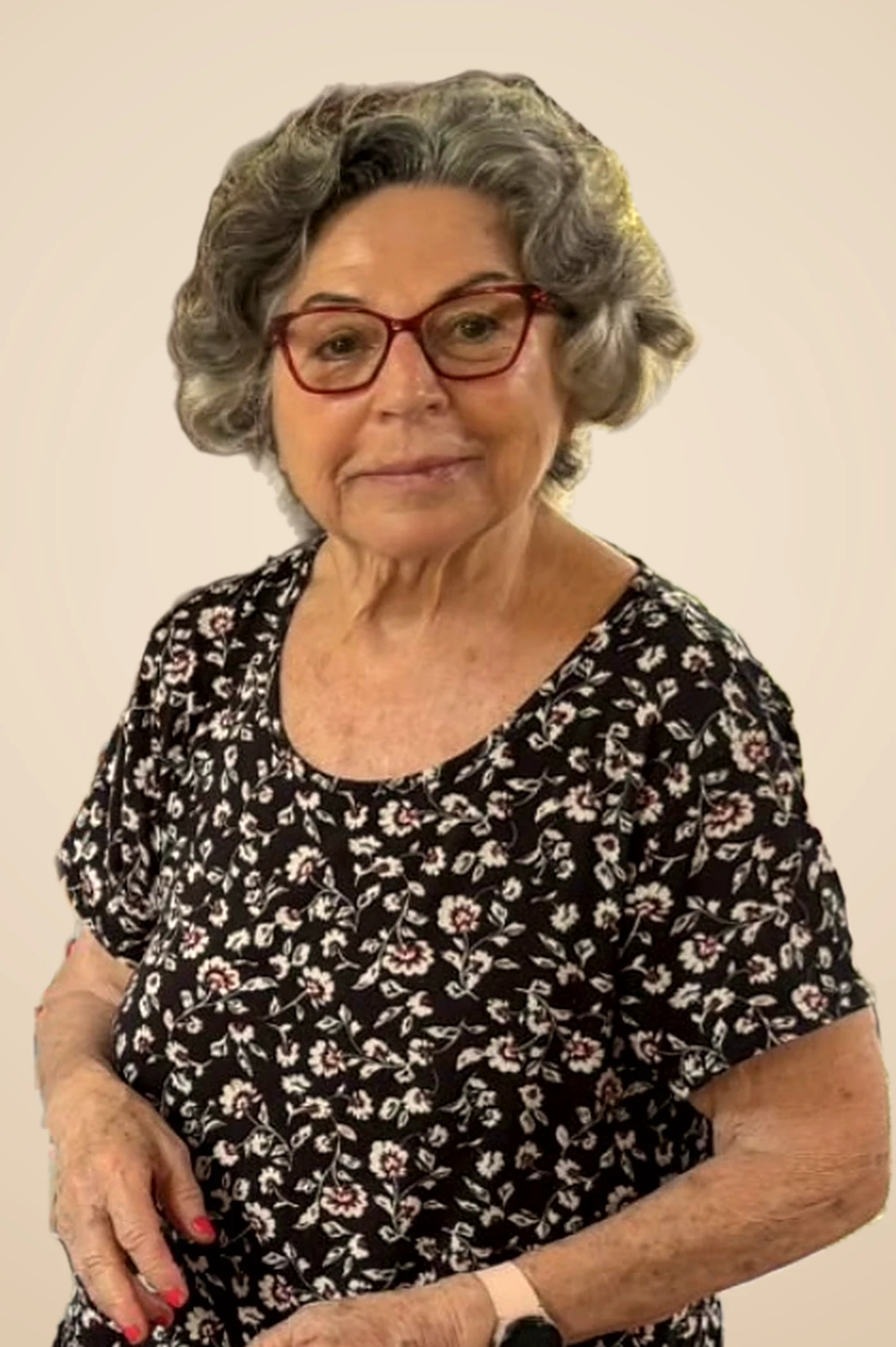 יהודית מיכאלי, עם משקפיים אדומים ושמלה פרחונית, מחייכת